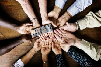 Many hands grabbing a woodblock that spells Pray