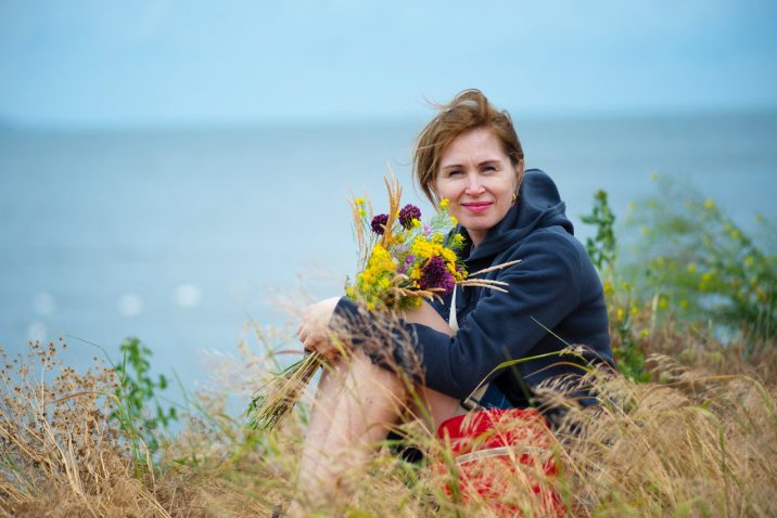 Middle aged woman holding flowers be ocean